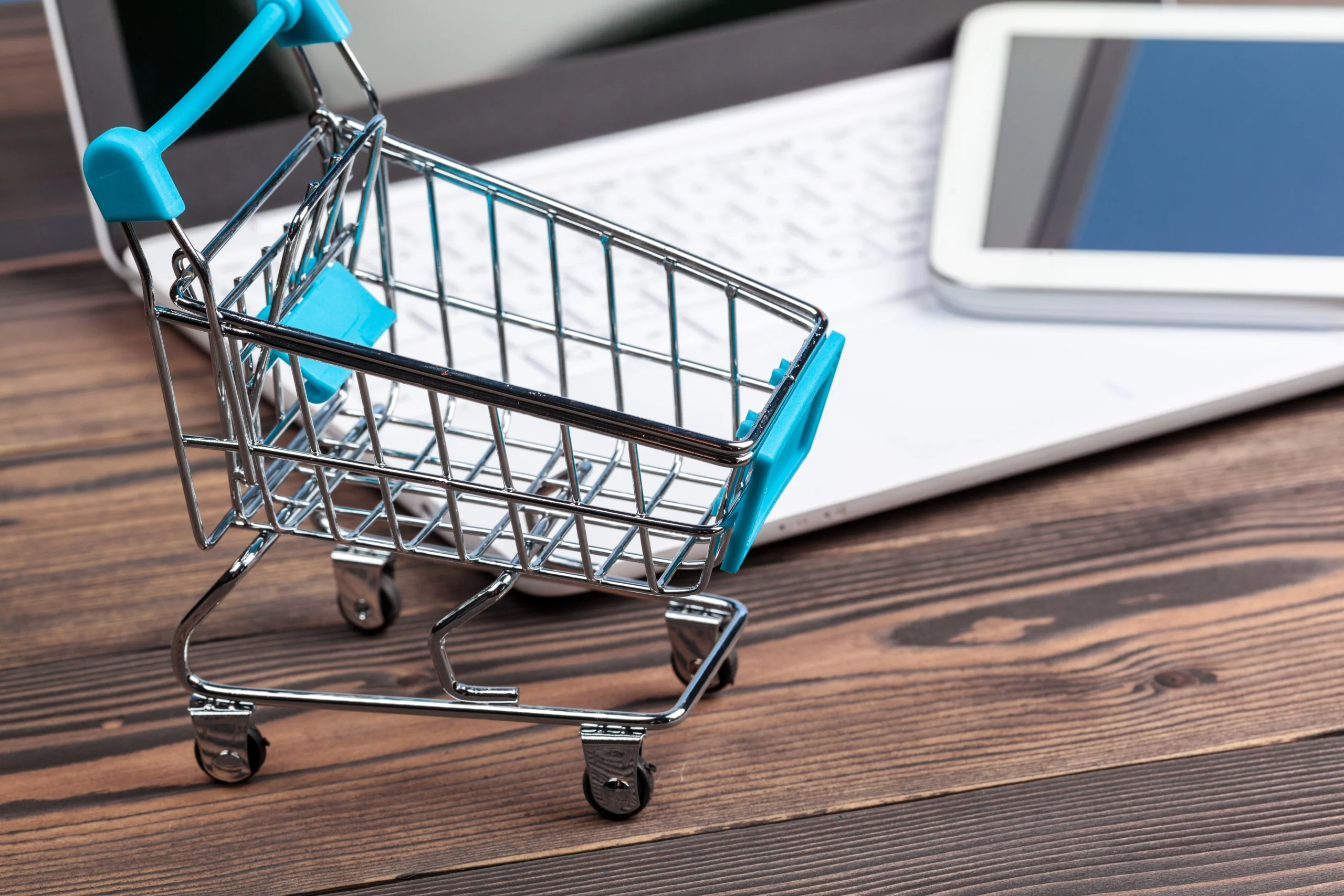 Miniature blue shopping cart resting next to a white laptop keyboard, highlighting e-commerce and SD-WAN for retail.