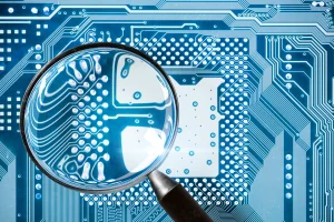 Magnifying glass inspecting a glowing blue circuit board to illustrate SD-WAN edge intelligence and deep packet visibility.