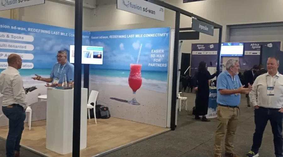 Professionals networking at an exhibition booth discussing last-mile SD-WAN deployment and connectivity. 