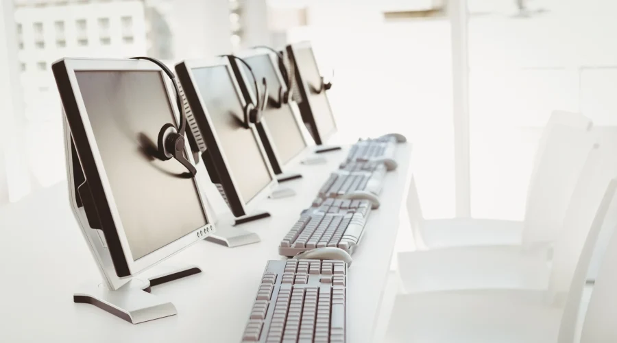 Empty modern office desks equipped with computer monitors and headsets, relying on SD-WAN for call centers.
