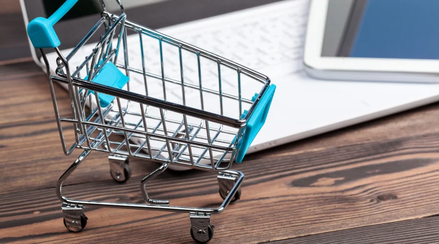 Miniature blue shopping cart resting next to a white laptop keyboard, highlighting e-commerce and SD-WAN for retail.